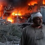 Раненый мужчина на фоне пожара и разрушений после атаки дронов