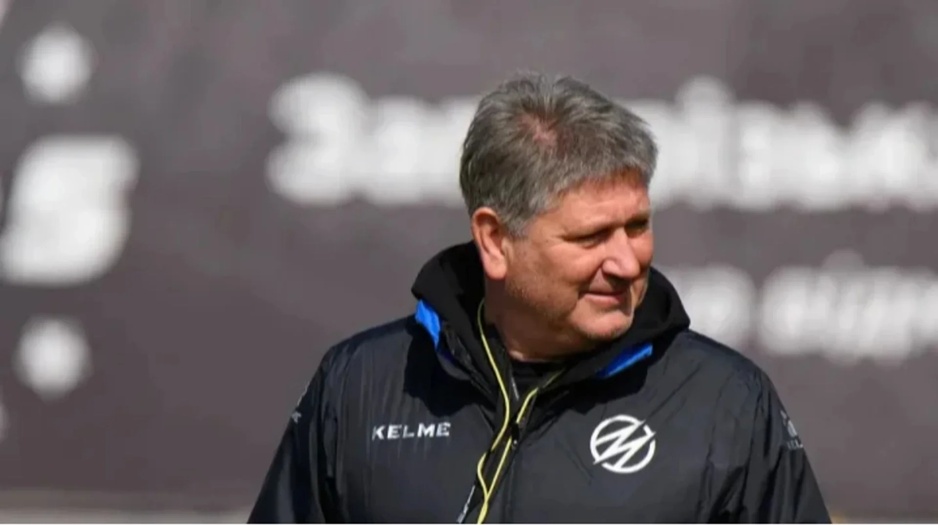 Сивий тренер у чорній куртці Kelme з круглим логотипом