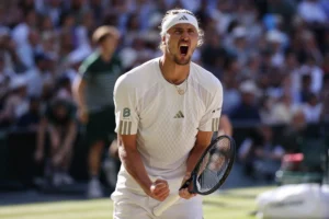 Тенісист у білій формі Adidas кричить і стискає кулак з ракеткою на трав’яному корті