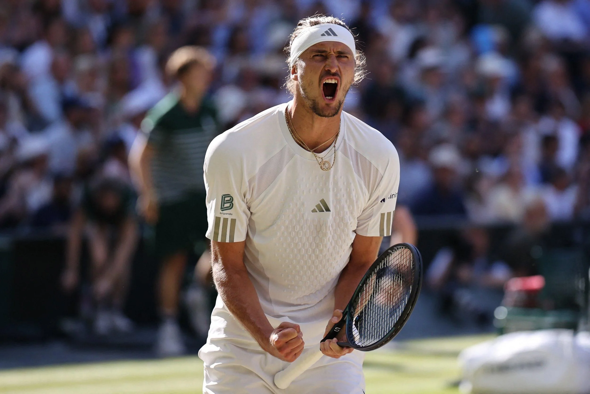 Тенісист у білій формі Adidas кричить і стискає кулак з ракеткою на трав’яному корті