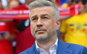 Чоловік у синьому піджаку на стадіоні серед уболівальників у червоному та жовтому