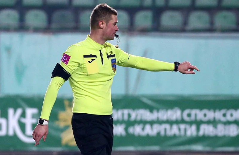 Футбольний арбітр у жовтій формі зі свистком вказує рукою на полі