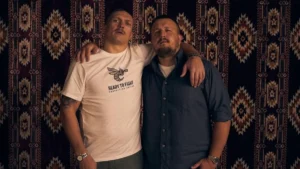 Двоє чоловіків обійнялися на тлі орнаментованого килима, один у боксерській футболці