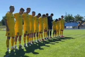 Гравці в жовтій формі стоять шеренгою на зеленому полі стадіону
