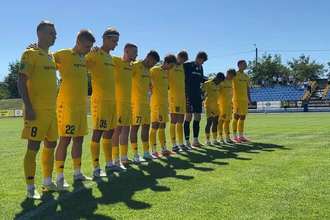 Гравці в жовтій формі стоять шеренгою на зеленому полі стадіону